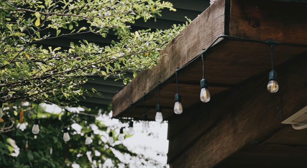 Dekorative pærer under kanten av en pergola i tre, omgitt av grønne planter